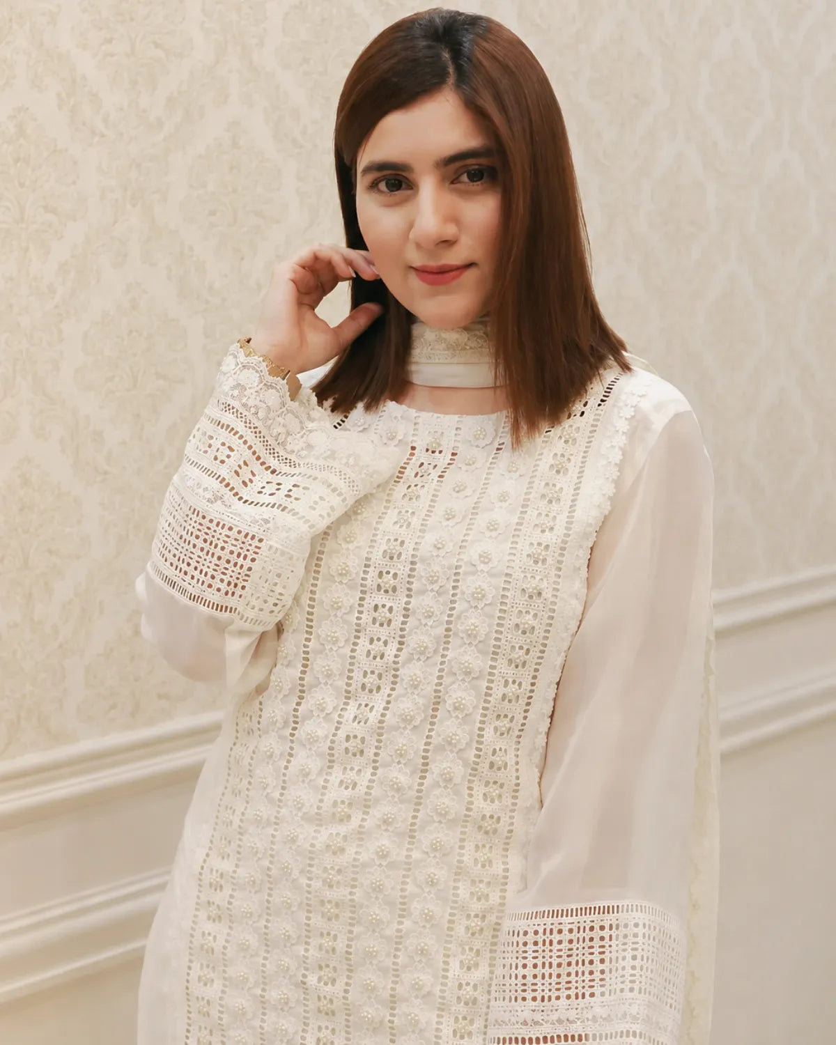 Woman wearing a white lace top against a light background